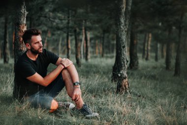 Ormanda düşünürken, çimlerin üzerine oturan genç adam