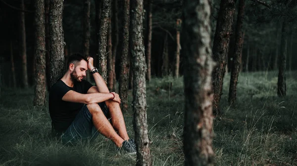 Young depressed man sitting alone in the forest