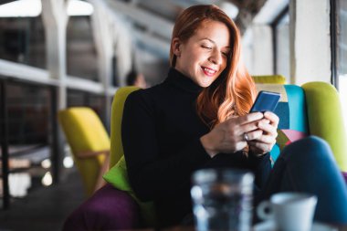 Kafede akıllı telefon kullanan genç bir kadın.