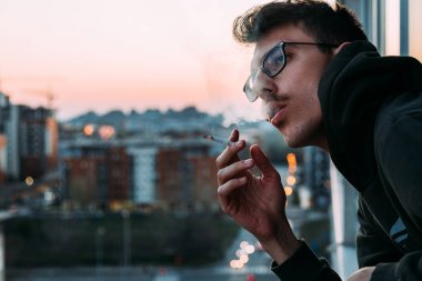 Young man smoking a cigarette on the balcony in sunset
