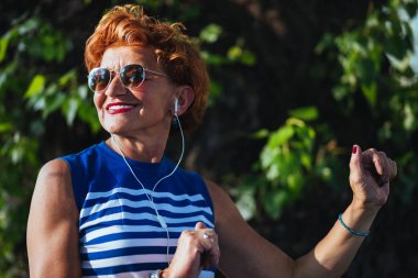 Parkta kulaklıkla müzik dinleyen olgun kadın
