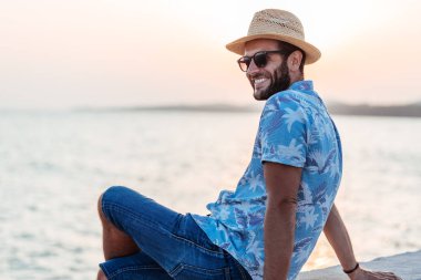 Genç adam deniz kenarında günbatımının tadını çıkarıyor.