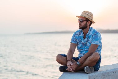 Young bearded man sitting by the sea in sunset clipart