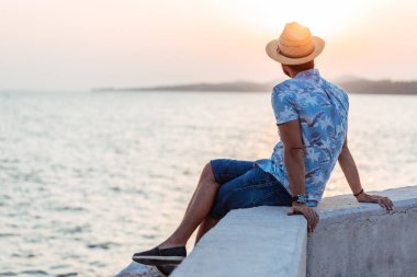 Genç adam deniz kenarında günbatımının tadını çıkarıyor.