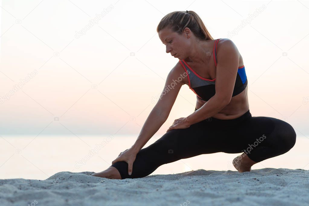 Young woman at the beach in sunset stretching after workout