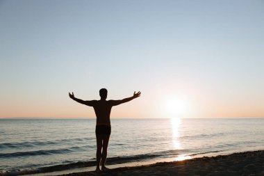 Denizden gün batımına bakan genç adam