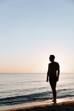 Sahilde günbatımının tadını çıkaran genç bir adamın silueti. 