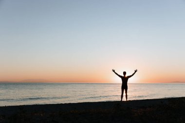 Sahilde günbatımının tadını çıkaran genç bir adamın silueti. 