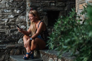 Yaşlı bir köyün merdivenlerinde akıllı telefon kullanan genç bir kadın.
