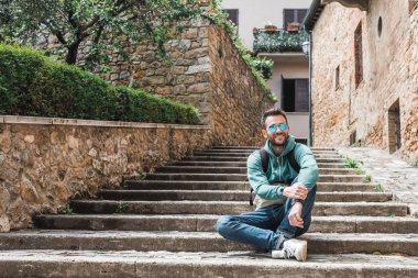 Genç gezgin, İtalya 'nın Toskana kentindeki eski San Quirico kasabasının merdivenlerinde oturuyor.