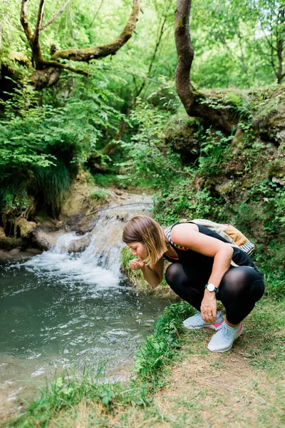 年轻的女性自然探险家从泉水中喝水 — 图库照片