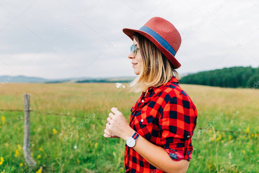 Young woman standing in a meadow with flower in her hands