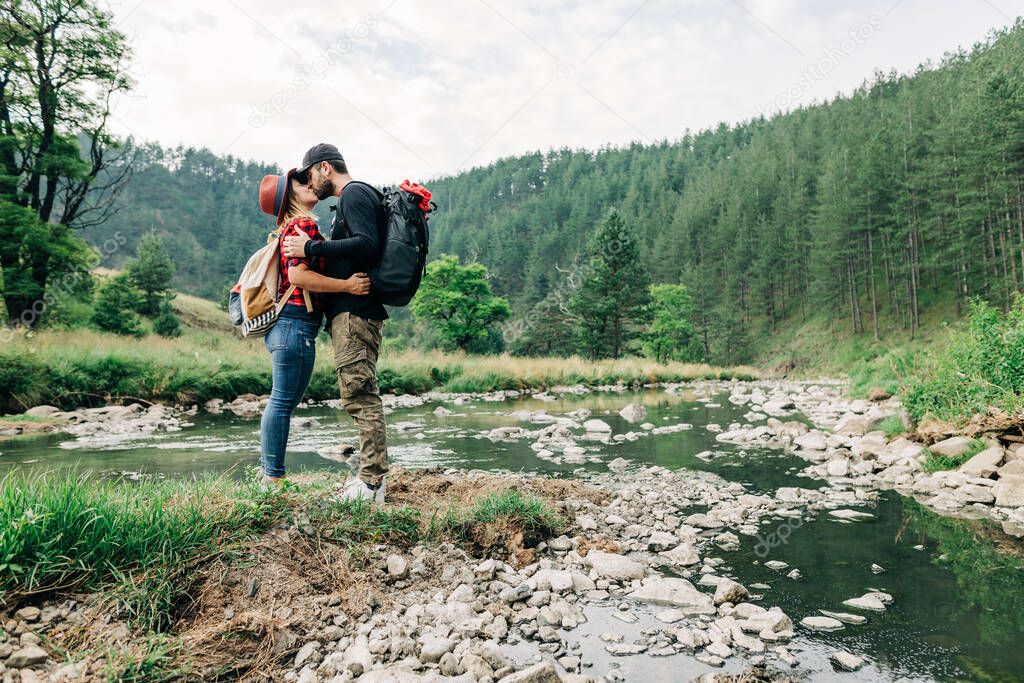 Young couple nature explorers kissing by the river in the mountains