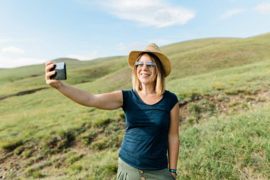 Yazın yamaçtaki çayırda selfie çeken genç bir kadın.