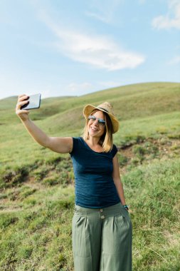 Yazın yamaçtaki çayırda selfie çeken genç bir kadın.