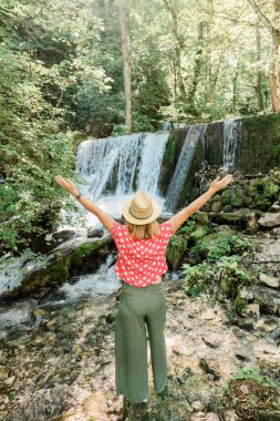 Şelalenin önünde duran genç kadın doğa kaşifi.