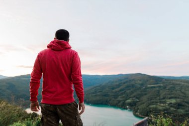 Genç adam gün batımında göl manzarasının tadını çıkarıyor.