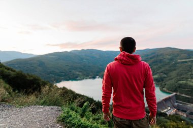 Genç adam gün batımında göl manzarasının tadını çıkarıyor.