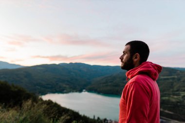 Genç adam gün batımında göl manzarasının tadını çıkarıyor.