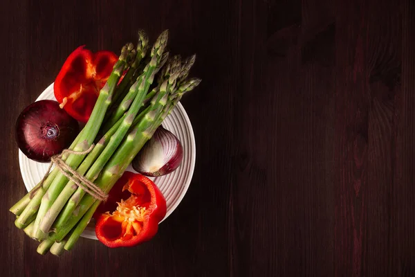 Taze biberli kuşkonmaz ve ahşap arka planda beyaz tabakta mor soğan. Düz yatıyordu. Alçak tuş.