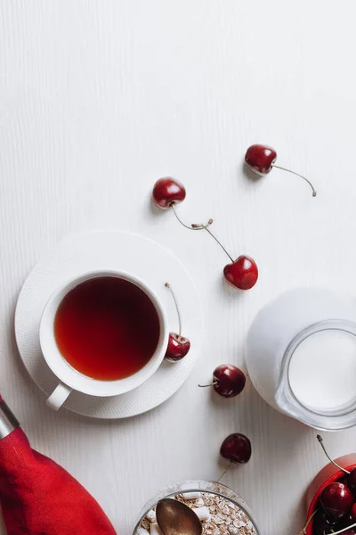 Sağlıklı kahvaltı, yulaf ezmesi, tatlı kiraz, kırmızı peçeteyle servis edilen çay ve süt, beyaz arka planda.. 