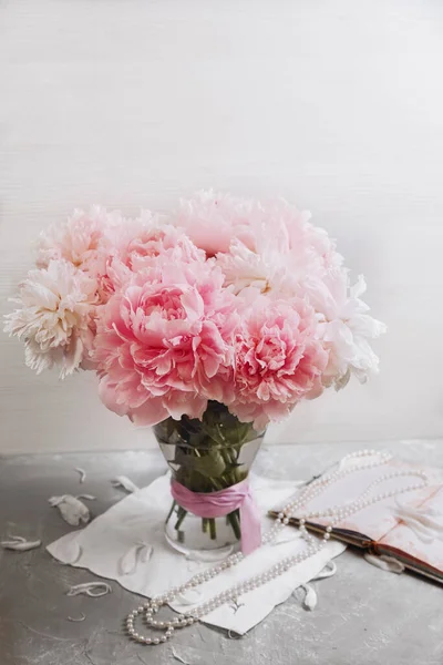 Cam vazoda şakayık buketi pembe şerit, inci kolye ve pembe not defteri. Yüksek tuş.