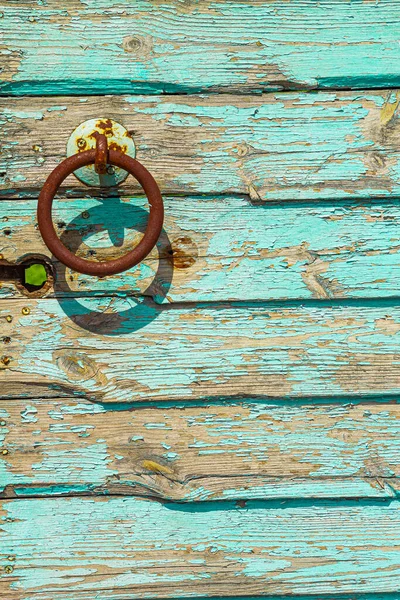 Kereste ağır yıpranmış kapı zemininde paslı bir kapı halkası ve mavi boyası var..