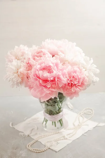 Cam vazoda pembe şeritli, inci kolyeli şakayık buketi. Yüksek tuş.