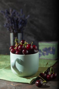 Yeşil peçetede lavanta buketi ile servis edilen taze kirazlarla dolu nane yeşili bir fincan. Alçak tuş.