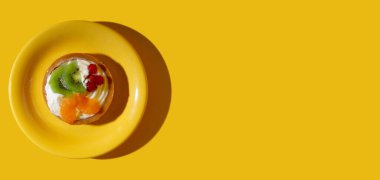 Süslü, kremalı, portakal dilimli, kivi dilimli, sarı fonda kırmızı frenk üzümlü bir pasta. Boşluğu kopyala.