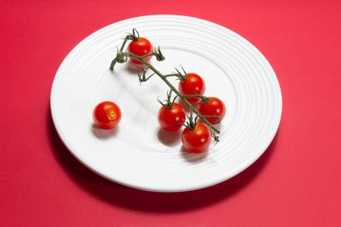  Beyaz tabakta canlı kırmızı arka planda olgun bebek domatesler. Yumuşak ışık. Yüksek çözünürlük.