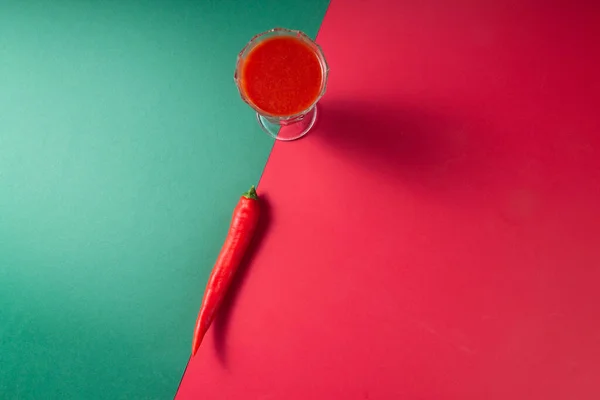 Bardakta domates suyu ve iki renkli kırmızı ve yeşil arka planda kırmızı biber. Bloody Mary kokteyli konsepti. Boşluğu kopyala.