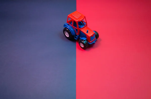 Colorful toy tractor in neon lights against blue and red background. Copy space.