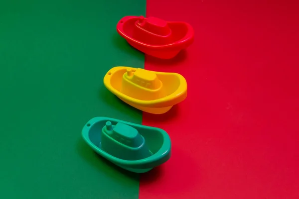 Kırmızı ve yeşil arka plana karşı üç kırmızı, sarı, yeşil plastik oyuncak tekne kavramı.