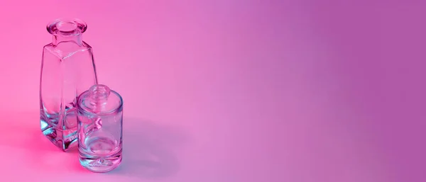 Bir silindirik yuvarlak tabanlı ve bir şekillendirilmiş kare kare kristal temiz boş cam şişelerle mavi ve pembe neon ışıklı renkli arka planda duran kavram. Pankart. Boşluğu kopyala.