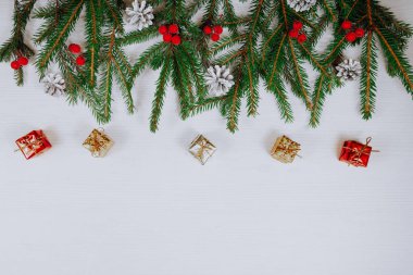 Beyaz ahşap arka planda yeni köknar dalları, süsler, koniler ve çeşitli renklerde mücevherlerden oluşan Noel sınırı. Boşluğu kopyala.