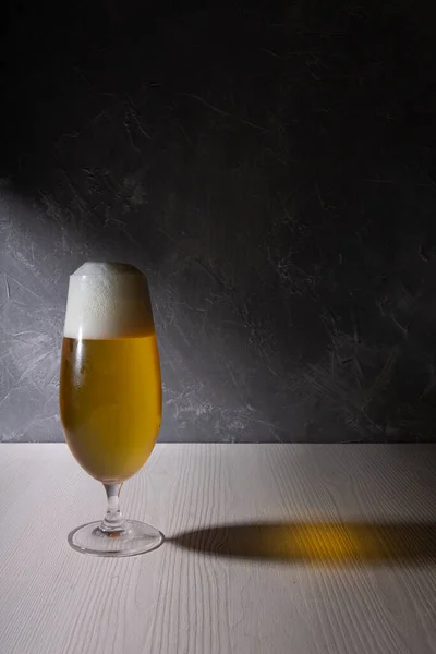 Koyu gri desenli arka plana karşı beyaz ahşap masada cam bardakta bira. Boşluğu kopyala.