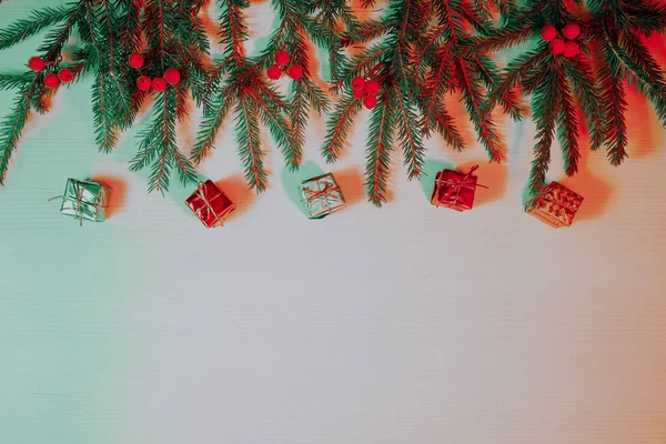 Beyaz ahşap arka plandaki Noel sınırı taze köknar dalları ve neon kırmızısı ve yeşil ışıklarla çeşitli renklerde süslemelerden oluşur. Boşluğu kopyala.