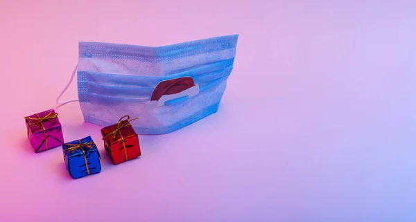 Coronavirus Noel ve yeni yıl konsepti tıbbi maske, Noel Baba 'nın şapkası, Noel süsü, neon ışıklı hediye kutuları. Boşluğu kopyala.