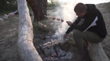 Yakışıklı adam ormanda ateşte et şişi pişiriyor.