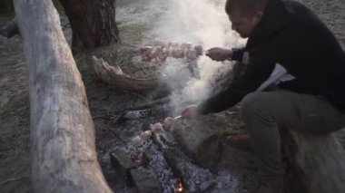 Yakışıklı adam ormanda ateşte et şişi pişiriyor.