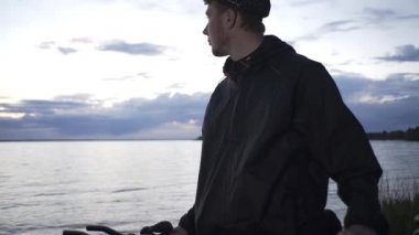 Yakışıklı kızıl saçlı adam nehrin kenarında duruyor ve gün batımını seyrediyor.