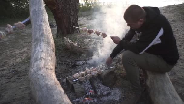 ハンサムな男は森の中の火の上で肉串を調理します — ストック動画