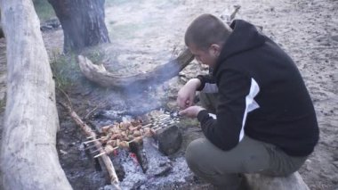 Yakışıklı adam ormanda ateşte et şişi pişiriyor.