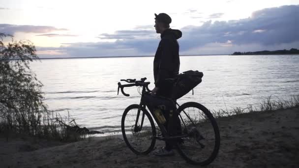 一个红头发的帅哥骑着自行车站在河边的森林里 看着夕阳西下 — 图库视频影像