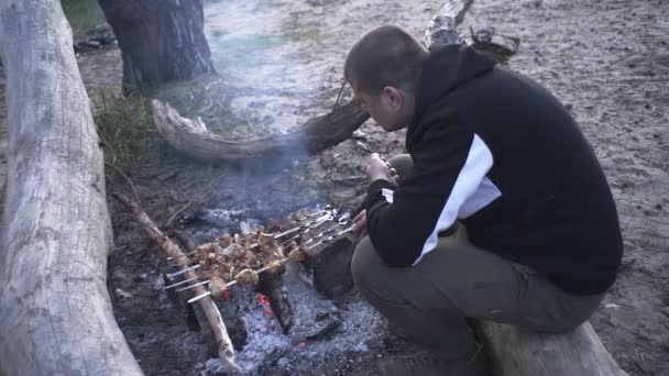 ハンサムな男は森の中の火の上で肉串を調理します — ストック動画