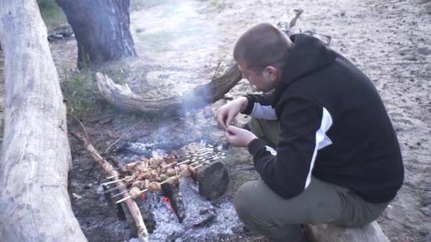 ハンサムな男は森の中の火の上で肉串を調理します — ストック動画