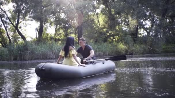 ハンサムな男と美しい女の子は夜に湖のゴムボートで泳ぐ — ストック動画