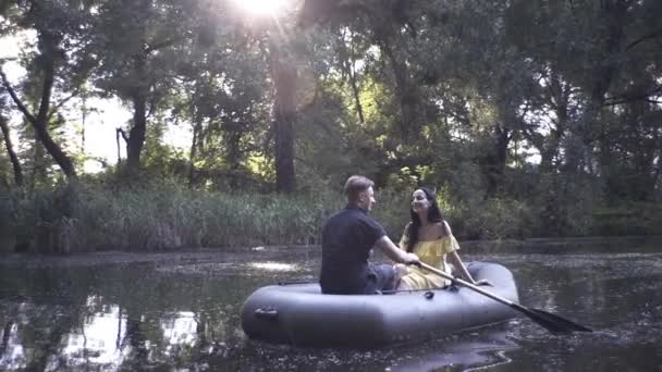 남자와 아름다운 여자가 저녁에 호수에서 고무배를 헤엄치고 있습니다 — 비디오