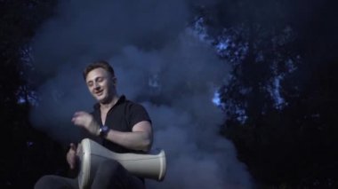 Yakışıklı adam bir peri ormanında ateşin etrafında oturur ve davul çalar